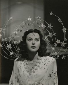 a woman with stars on her head wearing a white dress and gold necklaces,