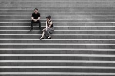 two people sitting on the steps in front of some stairs, one is looking down