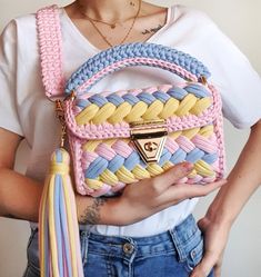 a woman holding a pink, blue and yellow purse with tassels on it