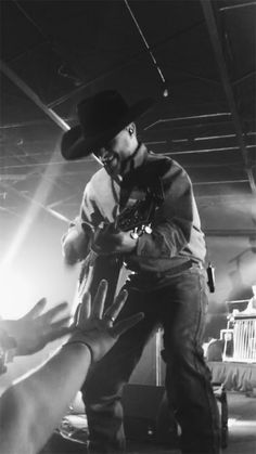 a black and white photo of a man with a cowboy hat on playing the guitar