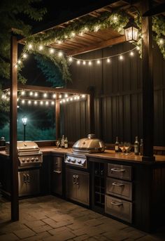 an outdoor kitchen is lit up at night with string lights on the roof and grill