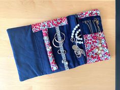 an assortment of jewelry is displayed on a wooden table with blue fabric and red flowers