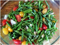 a glass bowl filled with green beans, tomatoes and other veggies on top of a wooden table