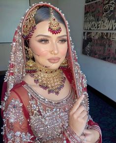 a woman in a red and gold bridal outfit with jewelry on her face, posing for the camera