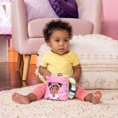 a small child sitting on the floor with a book in front of her and looking at the camera