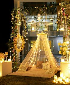 a bed covered in lights next to candles and flowers on the grass outside an apartment building