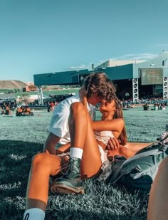 two people sitting on the grass in front of a stadium