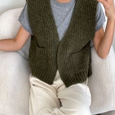 a woman sitting on top of a white chair wearing a green knitted sweater vest