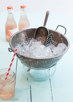 a metal colander filled with ice next to two bottles of soda and a straw