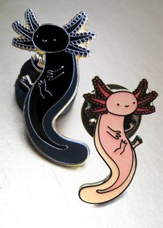 two pins with different designs on them sitting next to each other in front of a white surface