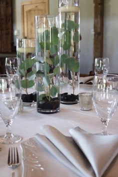 the table is set with silverware and glass vases filled with plants in them