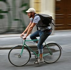 a man riding a bike down the street with a backpack on his back and wearing jeans