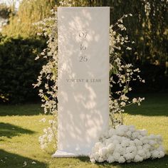 a large white sign sitting on top of a lush green field next to a bunch of flowers