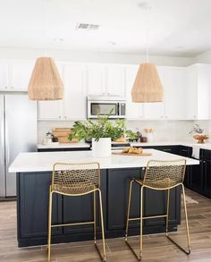 two chairs sitting in front of a kitchen island with white counter tops and black cabinets