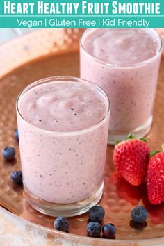 two glasses of fruit smoothie on a plate with strawberries and blueberries next to it