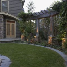 an outdoor patio with stone walkway and pergolated area in the foreground, surrounded by green grass