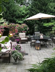 a patio with tables, chairs and umbrellas surrounded by flowers in the middle of it