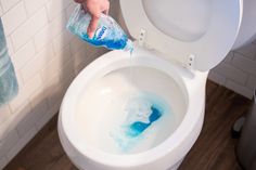 a person is cleaning a toilet with a blue sponge and a bottle of deterant