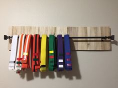 colorful belts hang on the wall in front of a wooden rack with black bar handles