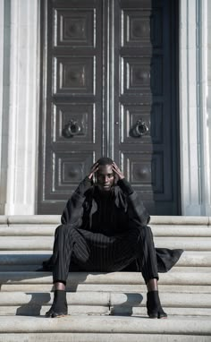 a woman sitting on the steps in front of a door with her hands to her head