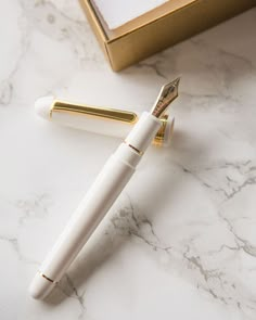 a white pen sitting on top of a table next to a gold and white box