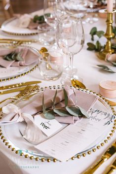 the table is set with gold and white place settings, napkins, and wine glasses