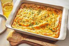 a casserole with cheese and herbs in a white dish next to a wooden spoon