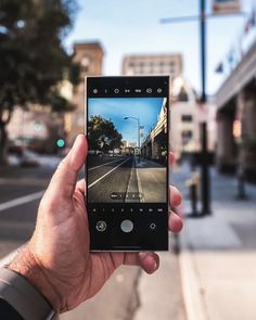 a person holding up a cell phone with a street in the background