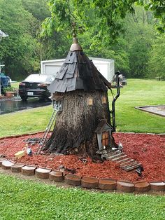 a tree house built into the side of a tree stump in a yard with red mulch on the ground