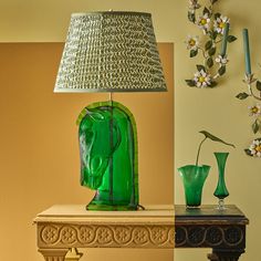 a green lamp sitting on top of a table next to vases and a lamp shade