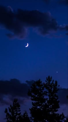 the moon and venus are seen through the clouds in this night time sky over some trees