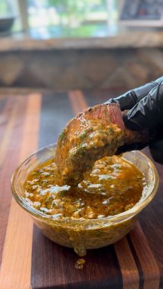 a person in black gloves is dipping some food into a glass bowl on a wooden table