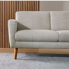 a gray couch sitting on top of a wooden floor next to a wall with wood slats