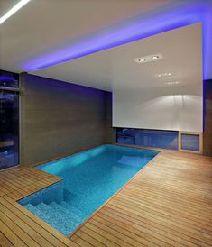 an indoor swimming pool with wooden floors and blue lights on the ceiling is seen in this image