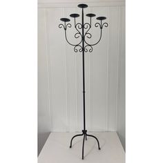 a black wrought iron coat rack with five candles on it's base and four lights on the top