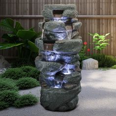 a water fountain in the middle of a garden with rocks and gravel around it, surrounded by greenery