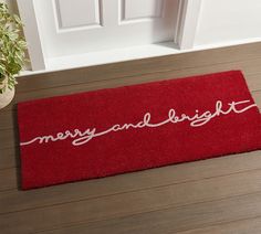 a red door mat with merry and bright written in white on the floor next to a potted plant