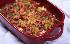 a red casserole dish with meat and cheese in it on a white cloth