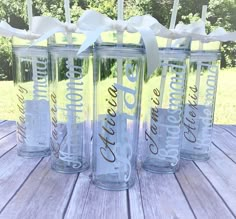 four clear tumblers with white bows are sitting on a wooden table in front of some trees