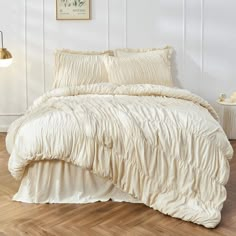 a bed with white sheets and pillows on top of wooden floor next to a wall