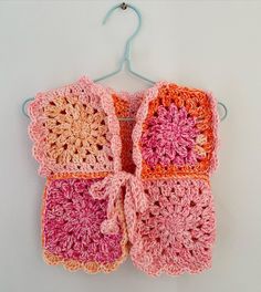 two crocheted squares are hanging on a clothes hanger, one is pink and the other is orange