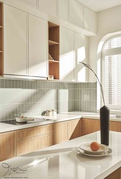 a kitchen with white counter tops and wooden cabinetry, along with a black vase filled with oranges