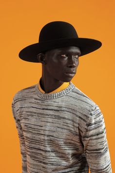 a man wearing a black hat and striped sweater with an orange background is looking at the camera