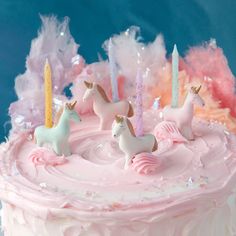 a pink cake with white frosting and unicorn figurines on top, surrounded by feathers