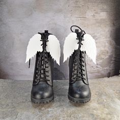 pair of black boots with white angel wings on them against a gray background, front view