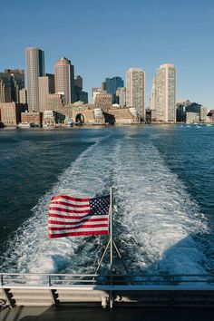 an american flag is waving on the back of a boat in front of a city skyline