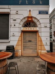 an old building with some tables and chairs in front of it, next to a closed door