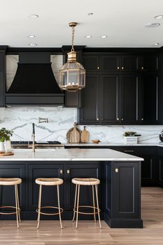 a kitchen with black cabinets and white marble counter tops, two stools in front of the island