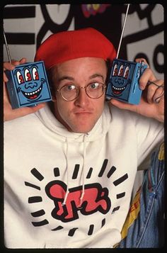 a man wearing glasses and a red hat holding up two blue boxes with faces on them