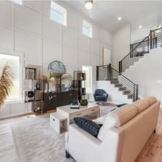 a large living room with white walls and wood flooring, stairs leading up to the second floor